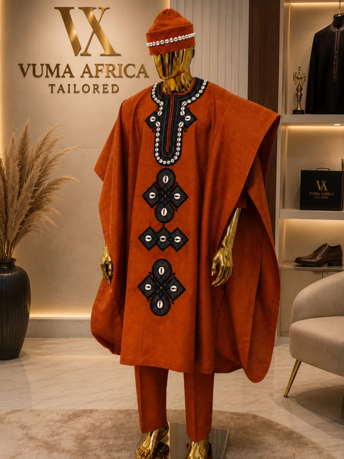 A gold mannequin wearing a burnt orange Agbada with black and white embroidery in a boutique.