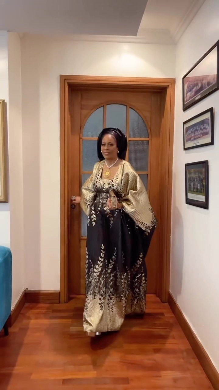 A woman wearing a black and gold patterned traditional African gown standing in a doorway.