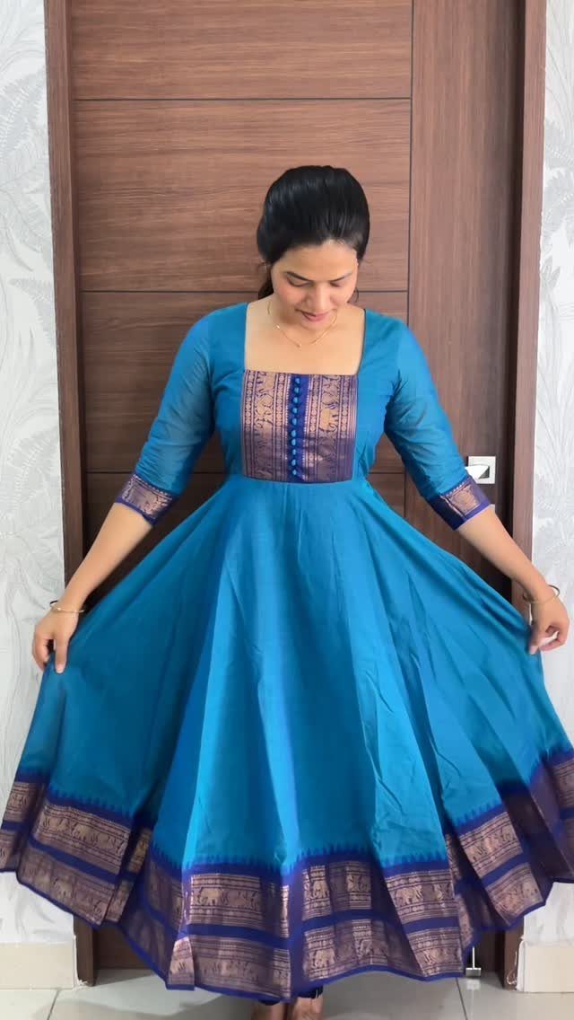 Woman wearing a long, flared teal blue Anarkali tunic with gold patterned borders.
