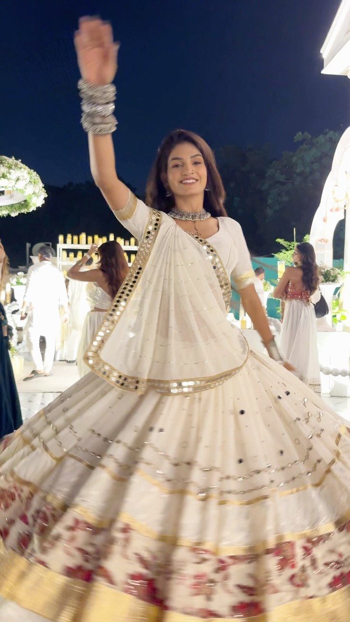 A woman dancing in a white and gold lehenga choli under the night sky.