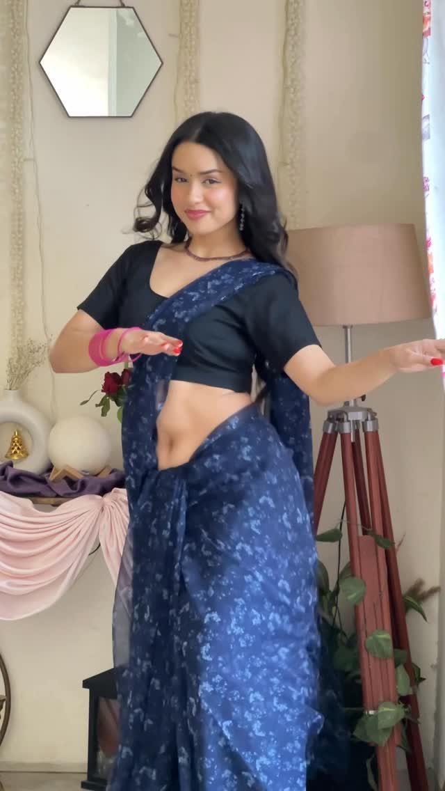 A woman posing in a dark blue floral patterned saree and a black blouse.