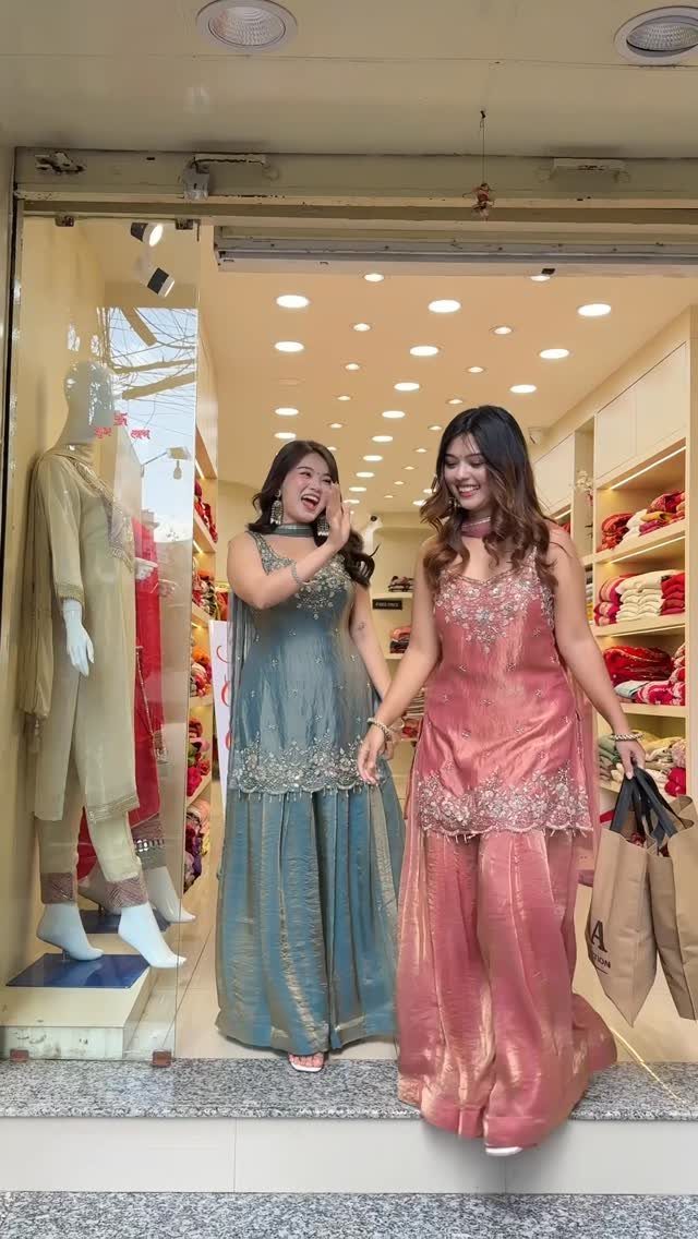 Two women walking out of a boutique wearing embroidered teal and pink sharara outfits.