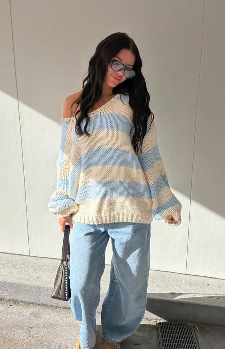 A woman wearing a striped oversized cream and blue knit sweater with wide-leg denim jeans.