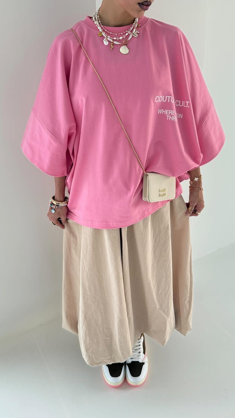A person wearing an oversized pink t-shirt and a beige midi skirt with white sneakers.