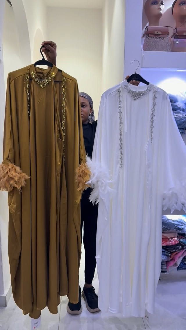 Two long dresses with feathered sleeve cuffs hanging on hangers in a clothing store.