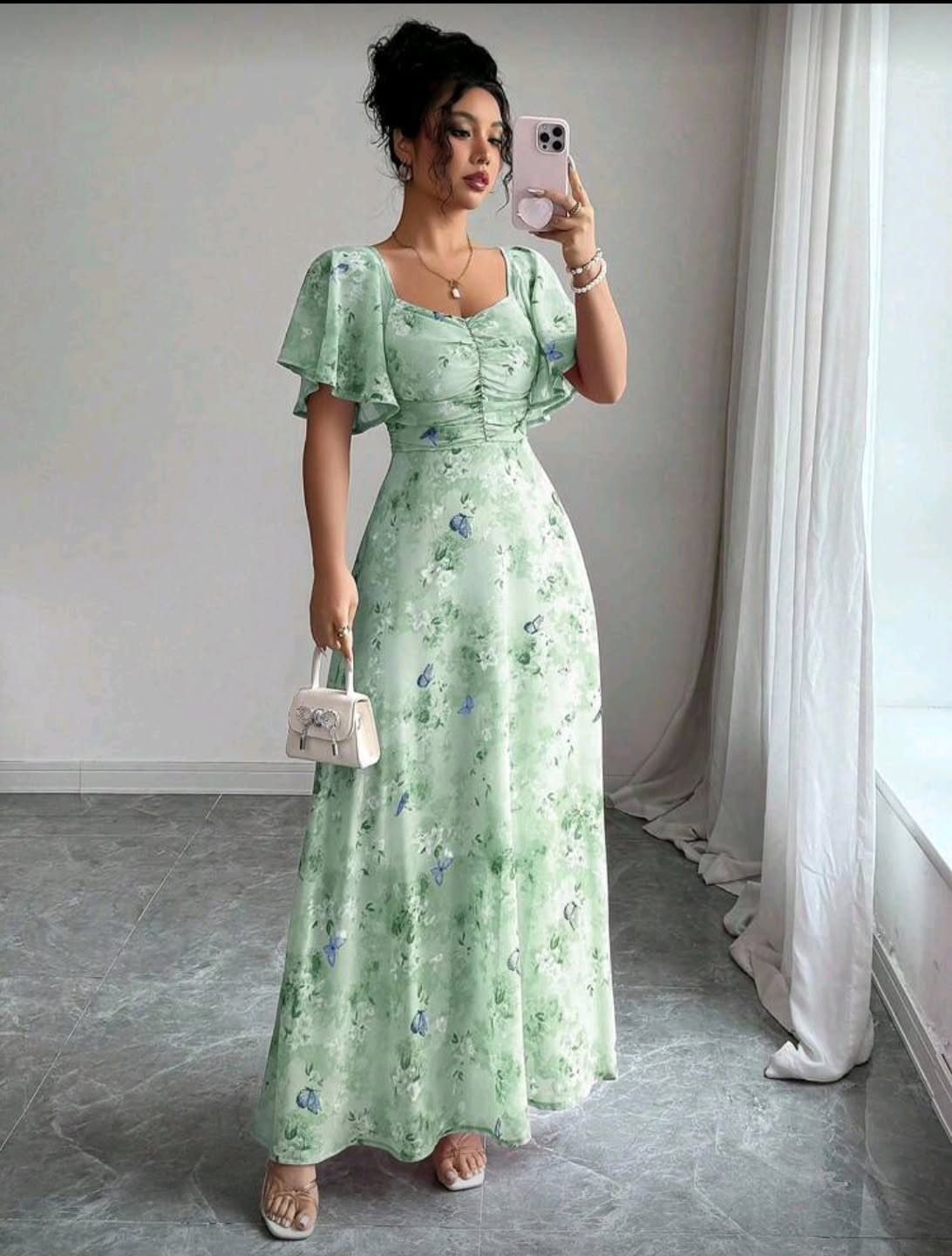 Woman in a green floral maxi dress with short, flowing flutter sleeves taking a selfie.