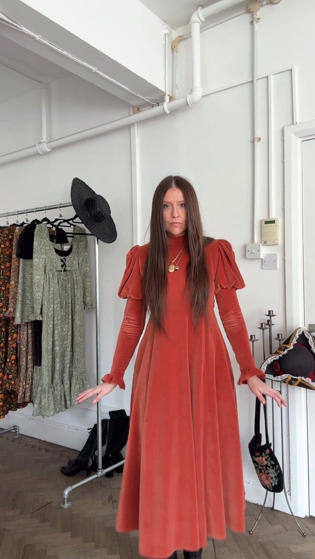Woman wearing a burnt orange velvet dress with distinctive puffed Juliet sleeves.