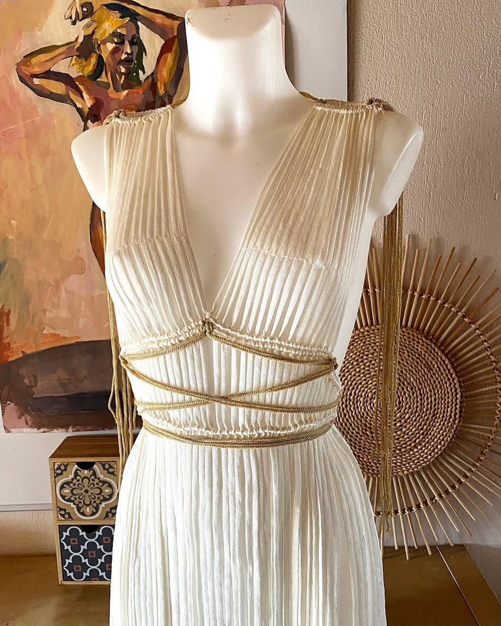 White pleated dress with deep V-neckline and gold cord accents on a mannequin.