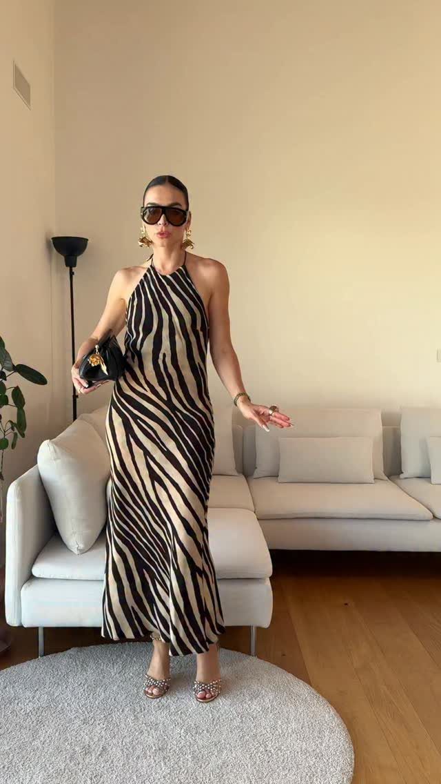 Woman posing in a long halter-neck dress featuring a bold black and tan zebra print.