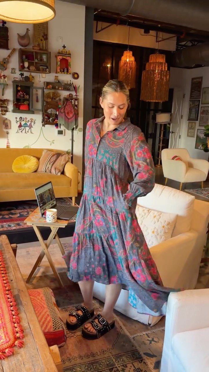 Woman wearing a patterned grey and pink midi dress standing in a bohemian living room.