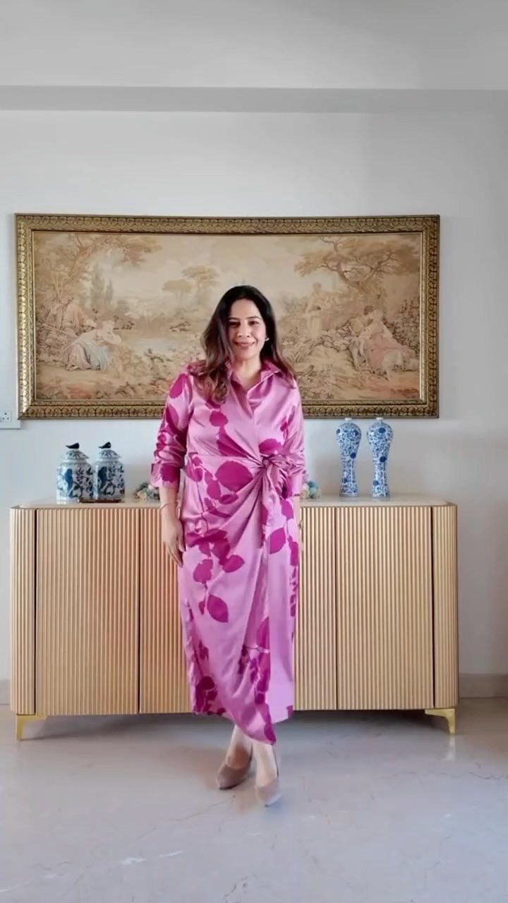 Woman wearing a pink floral print wrap dress standing in a room with a sideboard.