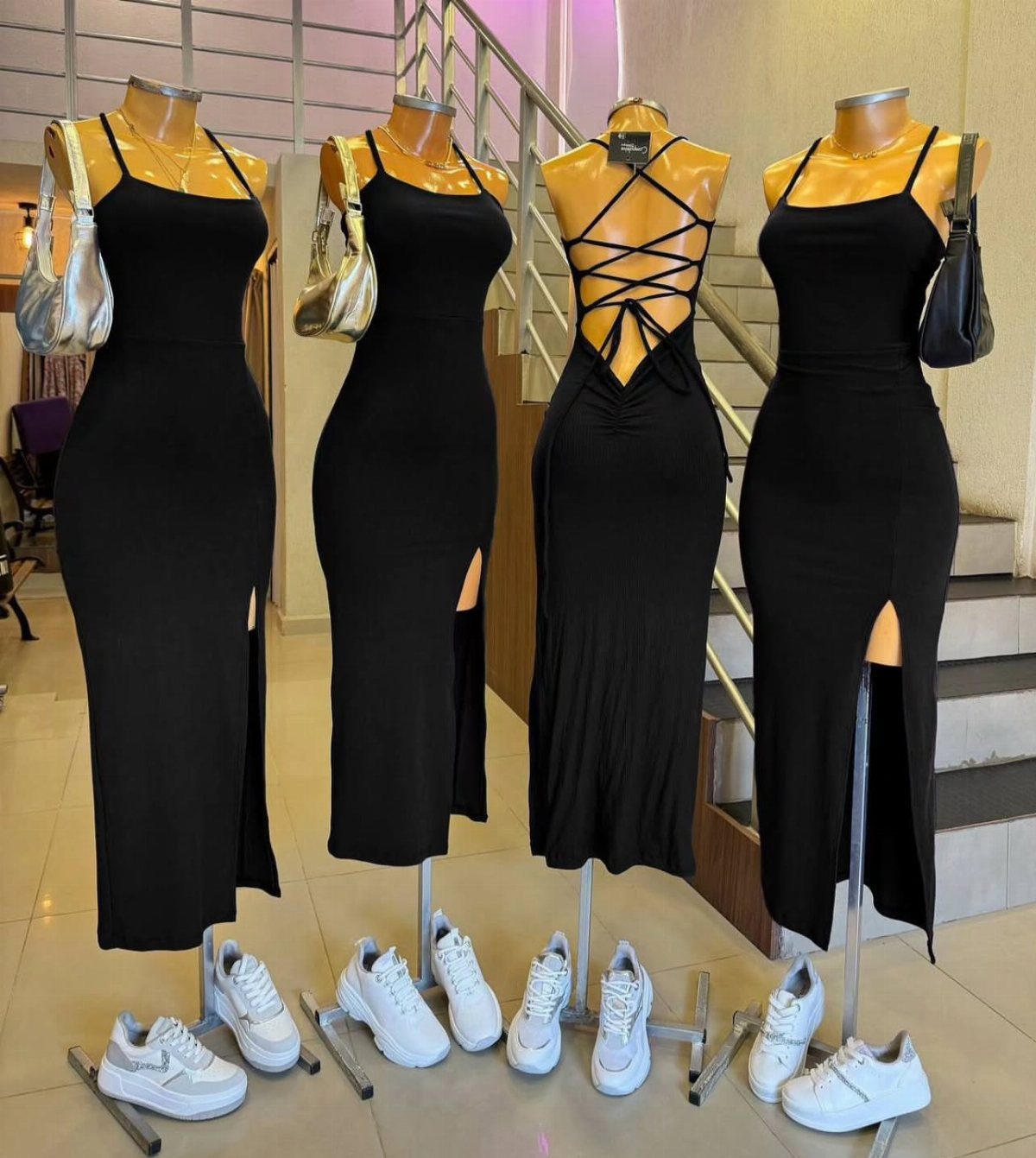Four black mannequins wearing long, form-fitting maxi dresses with side slits and white sneakers below.