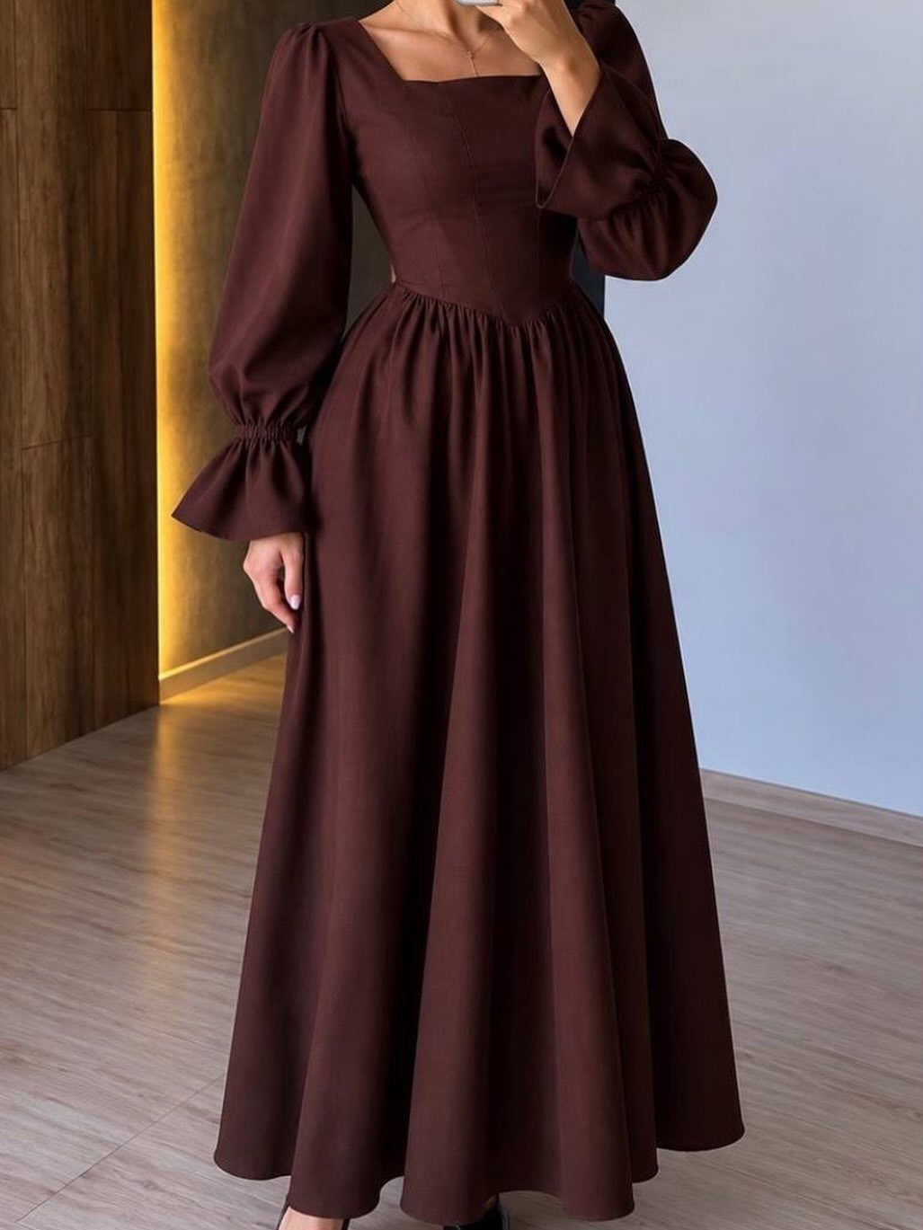 A person wearing a long-sleeve dark brown maxi dress with voluminous puff sleeves.