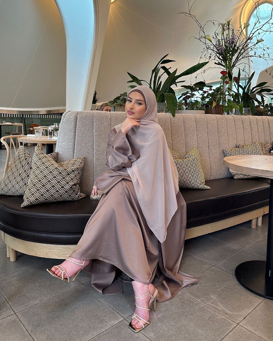 Woman in a flowing taupe neutral maxi dress sitting on a restaurant banquette.