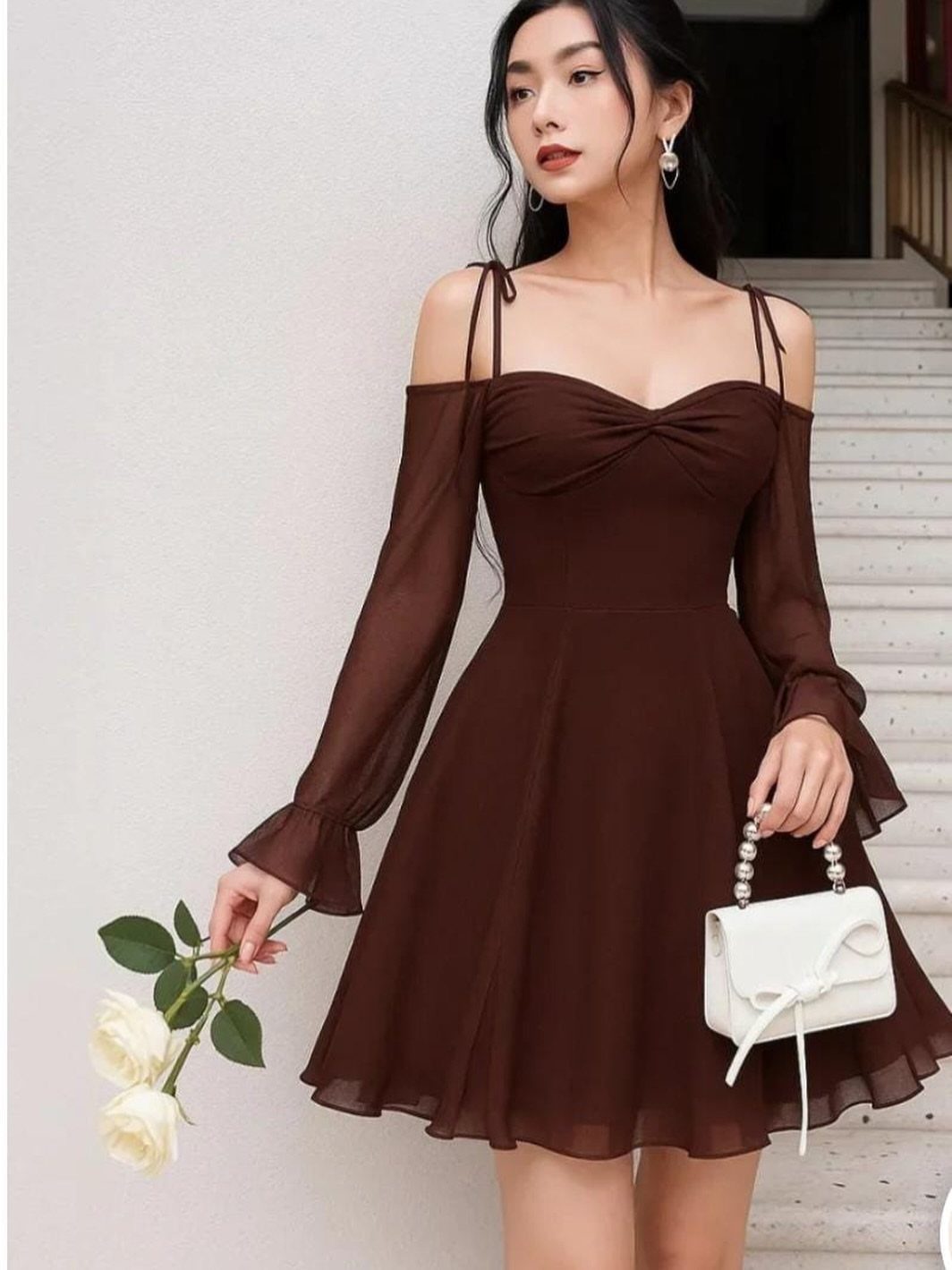 Woman in a dark brown long-sleeved mini dress holding white roses and a small white purse.