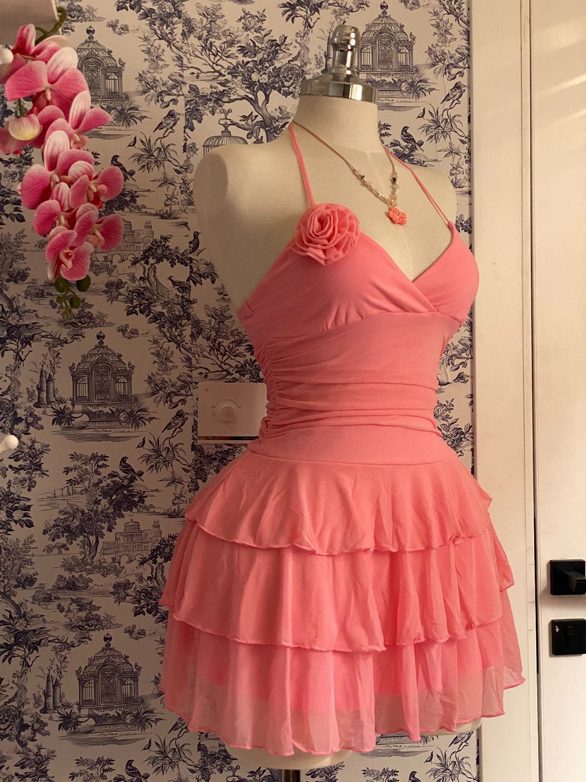 A pink halter mini dress with a tiered, layered skirt displayed on a white mannequin.