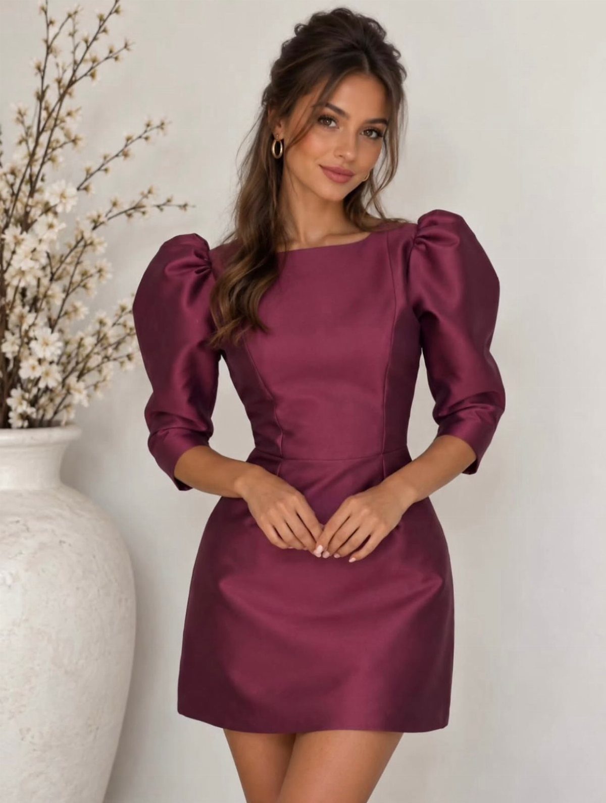 A woman posing in a maroon satin short dress with puffed sleeves against a white background.