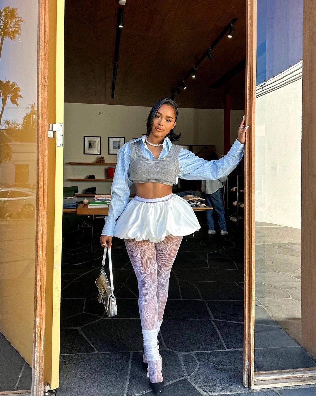 A woman posing in a light blue bubble skirt, grey crop top, and patterned white tights.