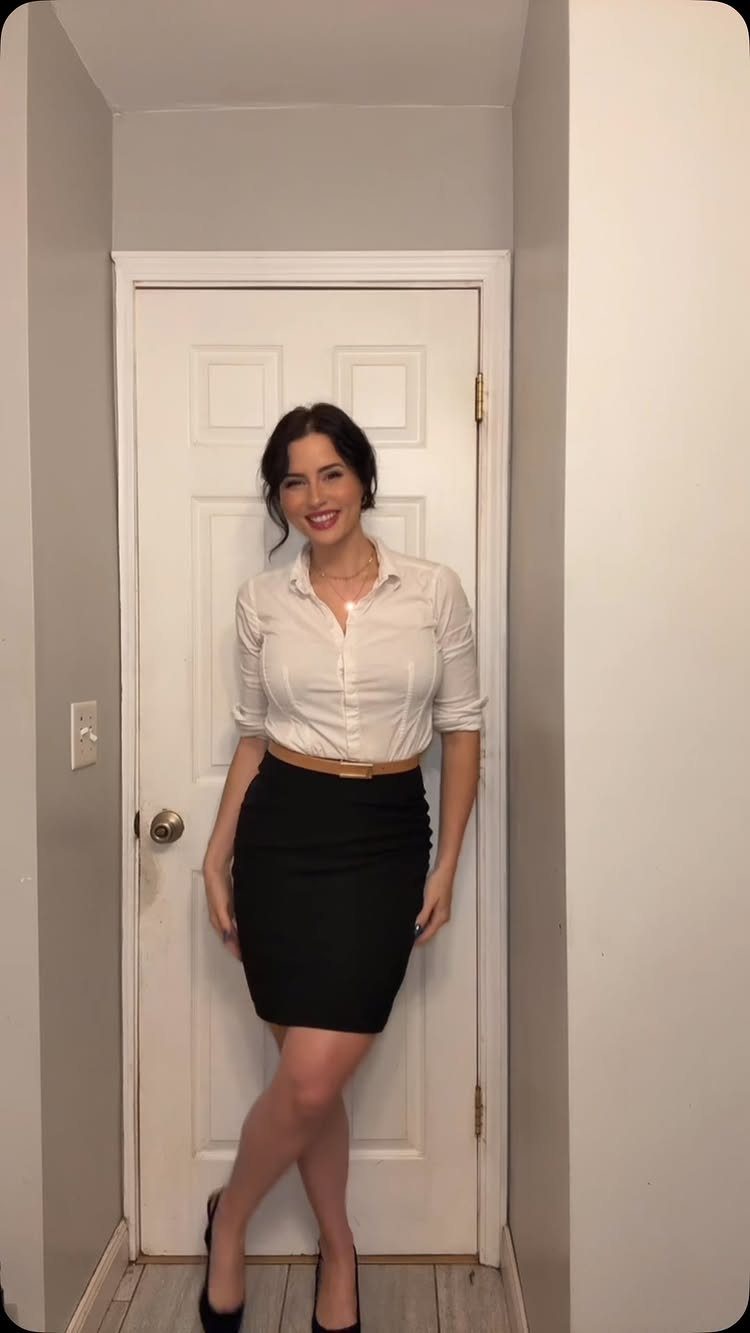 A woman posing in a white shirt and a black pencil skirt against a white door.