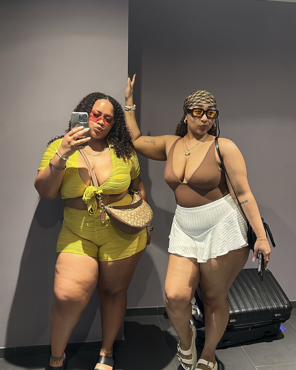 Two women posing in a mirror selfie wearing colorful summer outfits and sunglasses.