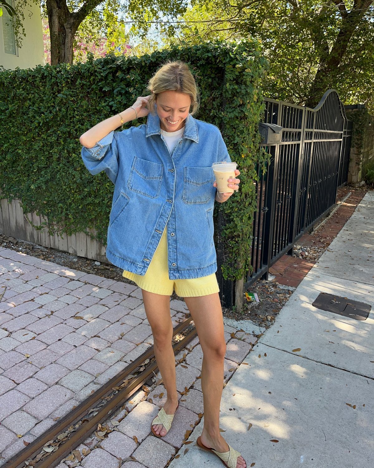 A woman wearing an oversized light blue denim jacket and yellow shorts standing outdoors.
