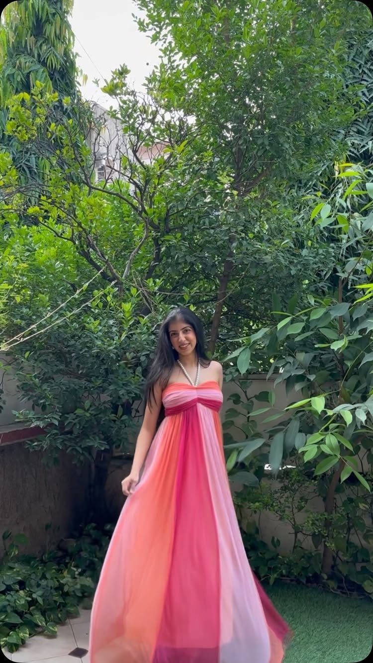 A woman wearing a colorful pink and orange ombre strapless maxi dress in a garden.