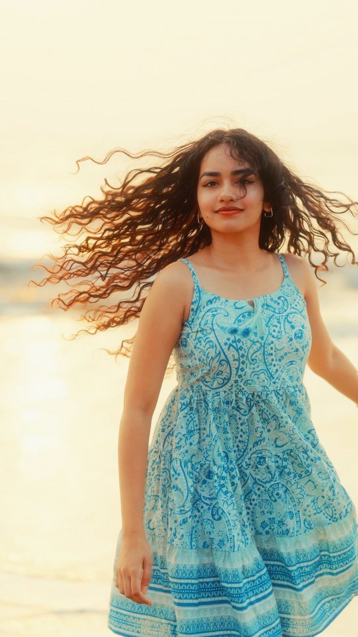 A woman with long wavy hair wearing a blue patterned sundress at sunset.