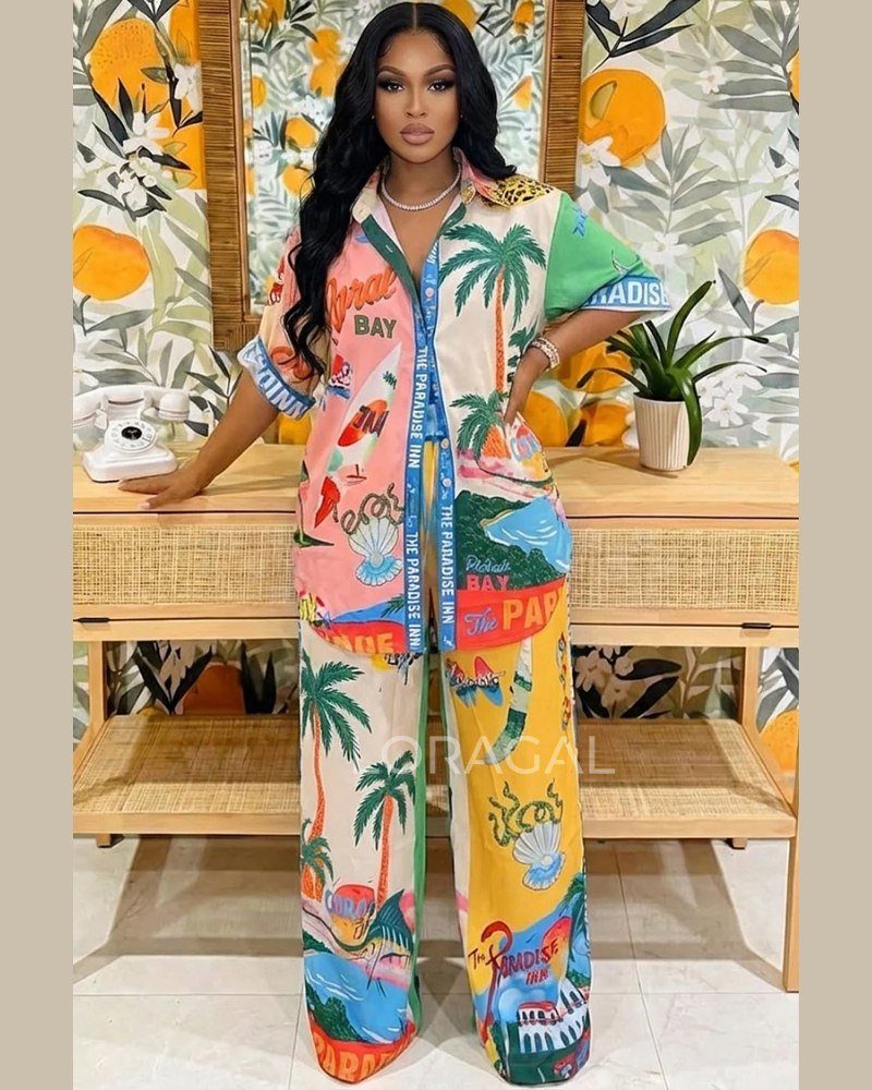 Woman wearing a colorful tropical print shirt and matching wide-leg trousers standing in front of a sideboard.