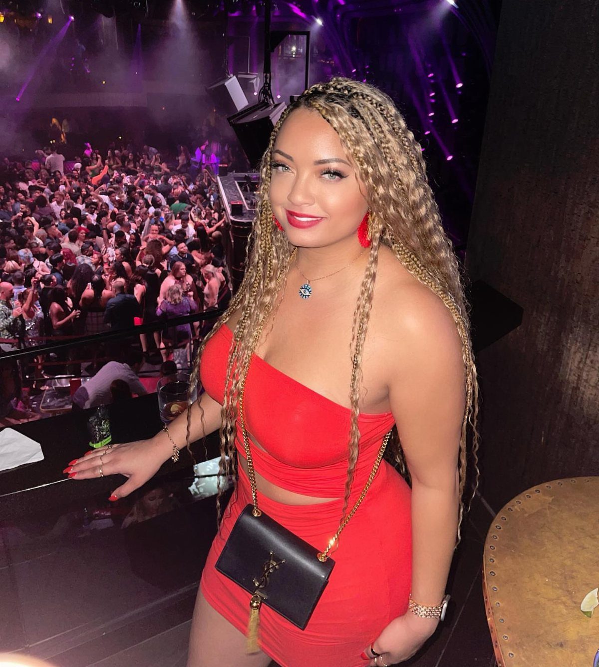 A woman with long blonde braids wearing a red cutout dress in a crowded nightclub.