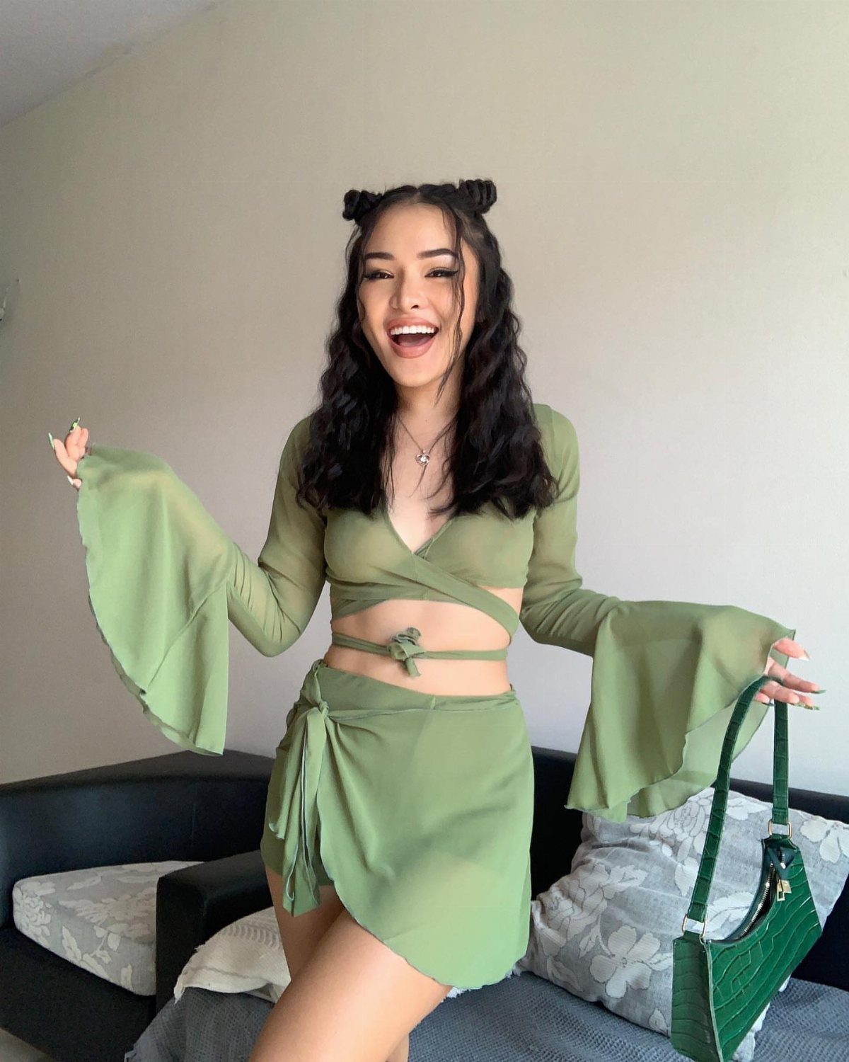 A smiling woman in an olive green two-piece set with bell sleeves and a matching skirt.