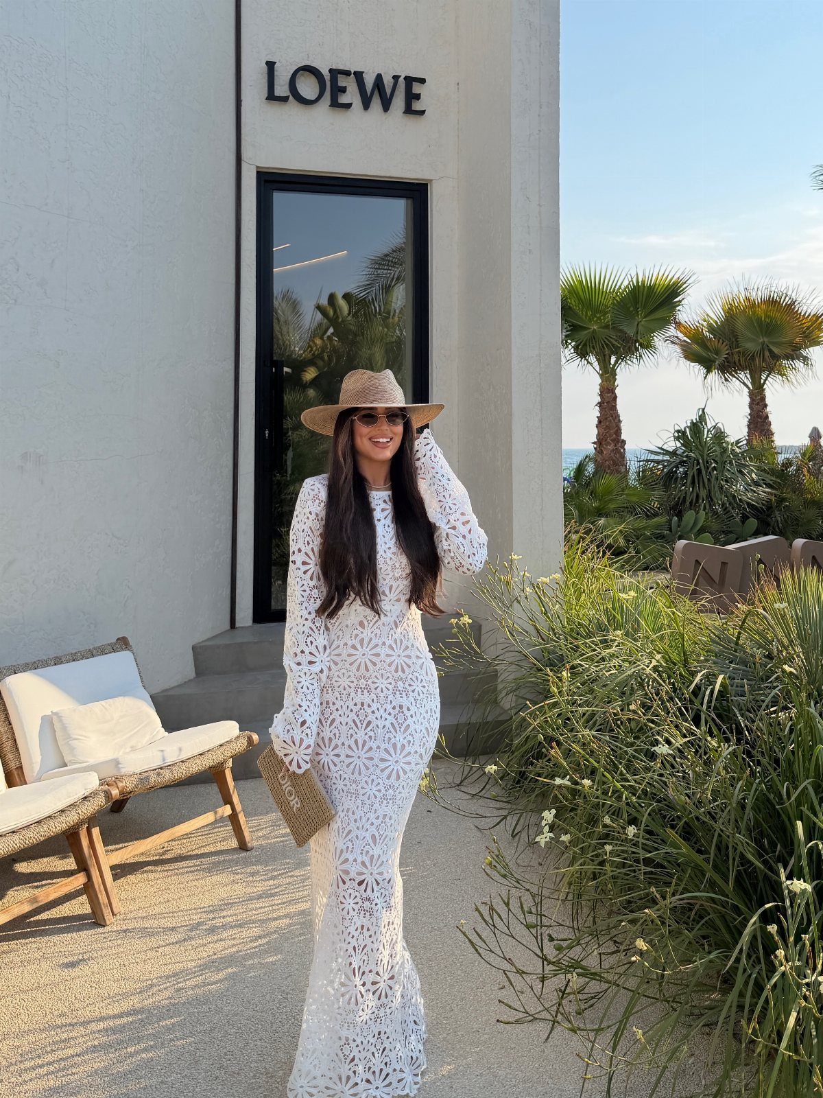 Woman in a white lace maxi dress and straw sun hat standing outdoors.