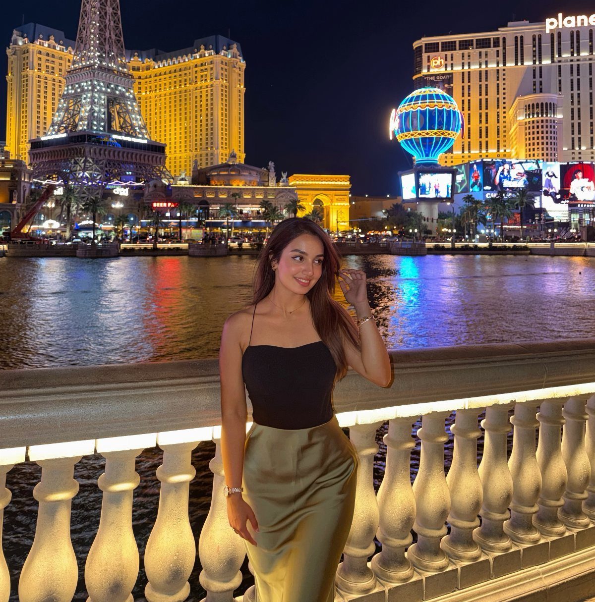A woman in a black top and gold satin skirt posing by a Las Vegas waterfront at night.