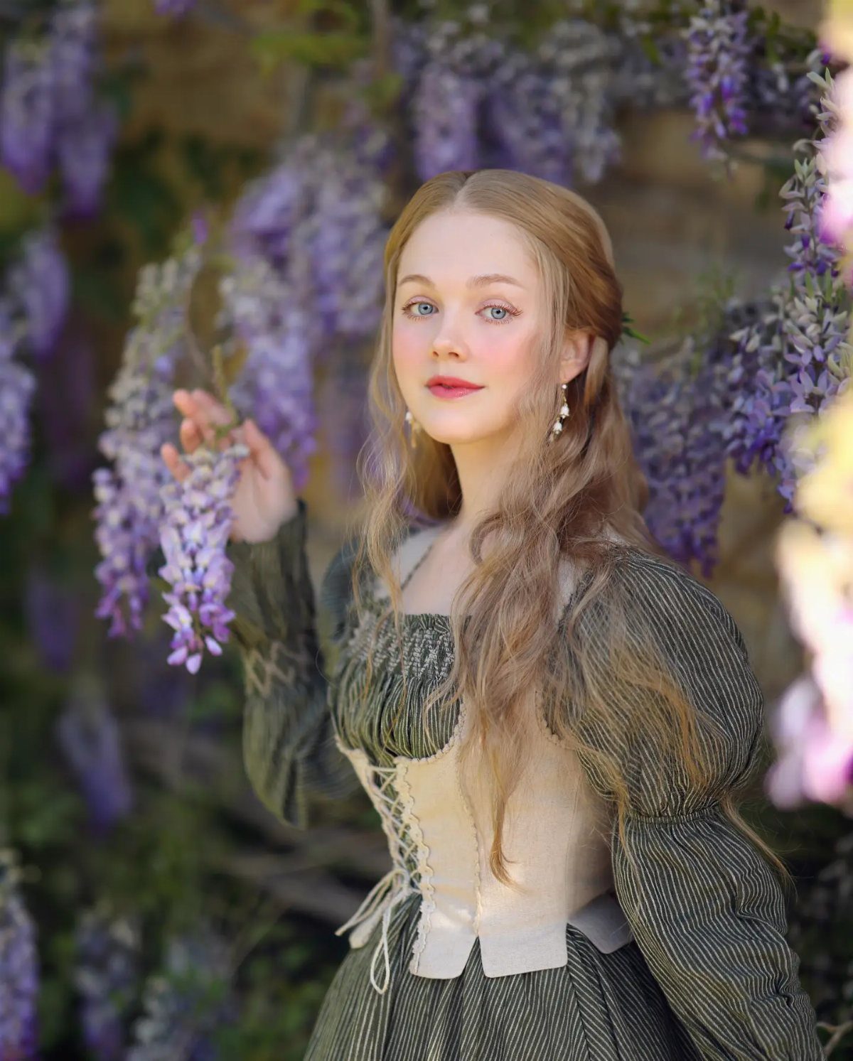 A young woman in a vintage-style corset dress posing among purple wisteria flowers.