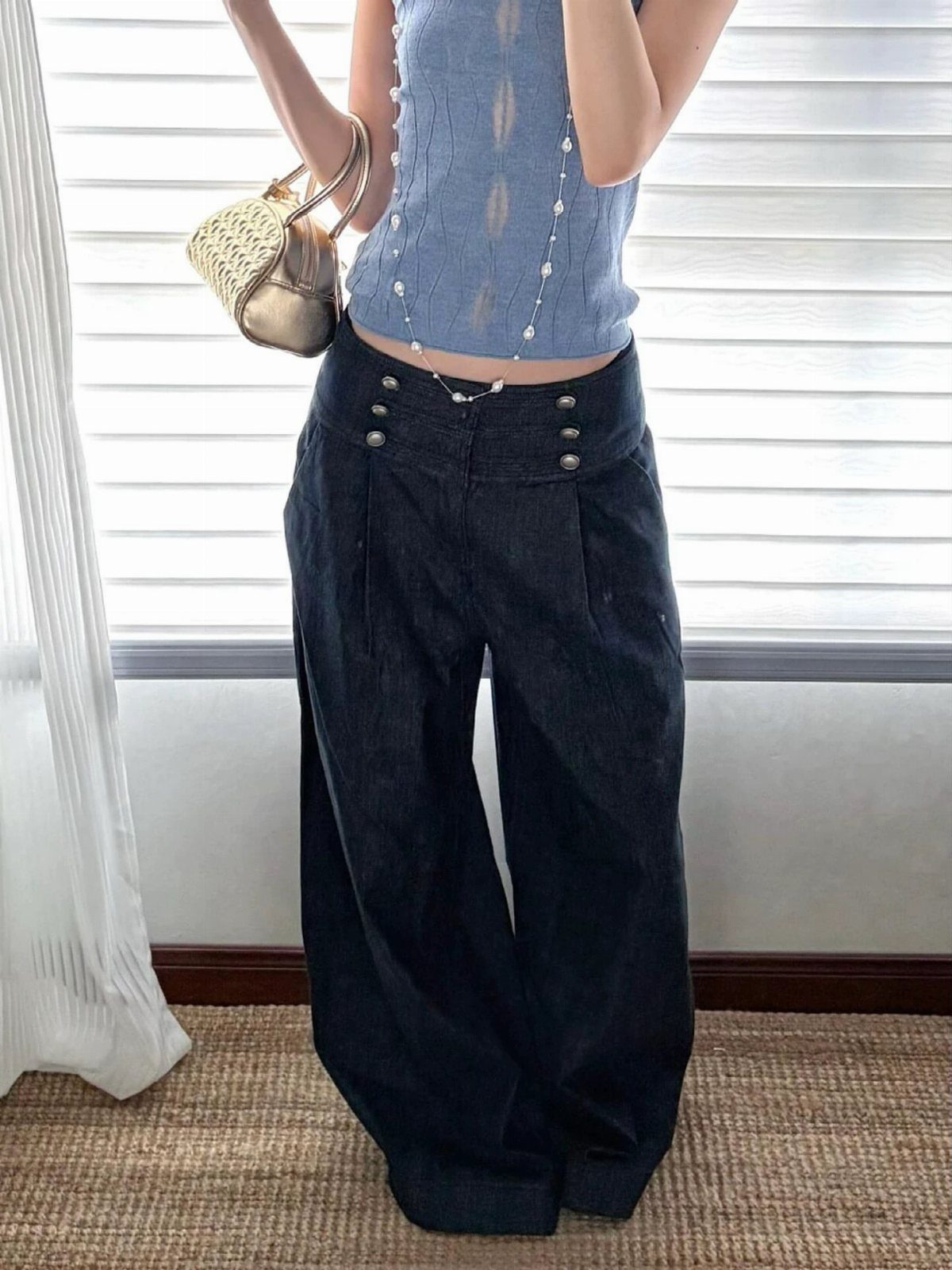 Person wearing high-waisted dark denim wide-leg pants with gold button details and a blue top.