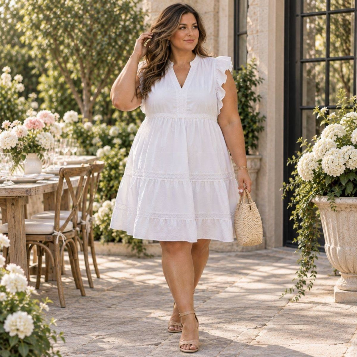 A woman walking in a white ruffled V-neck tiered dress on a sunny patio.