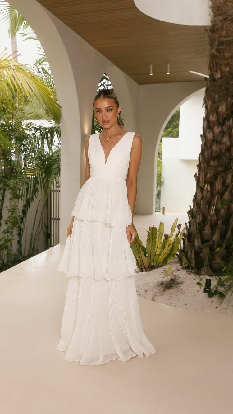 A woman posing in a long white tiered maxi dress on a sunny patio.