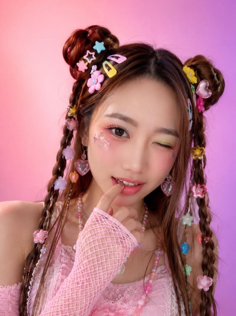 A young woman with colorful butterfly hair clips in her braided hair against a pink background.