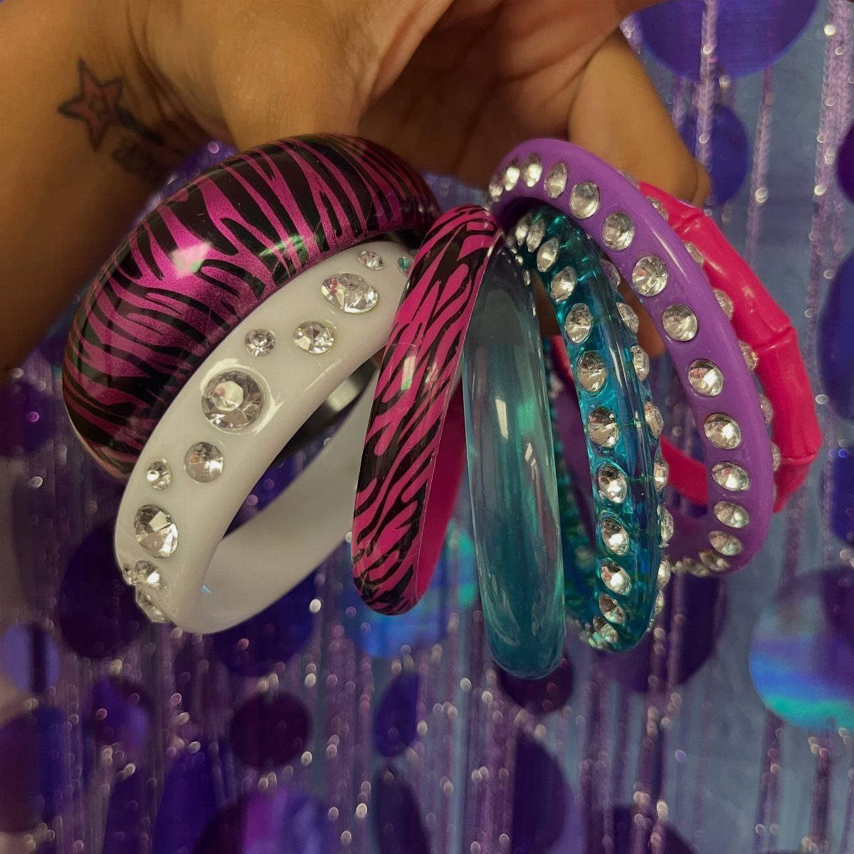 A hand holding various colorful, patterned, and rhinestone-embellished chunky bangles.