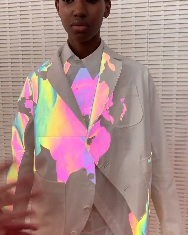 Person wearing a white suit jacket decorated with large, iridescent holographic patches reflecting colorful light.