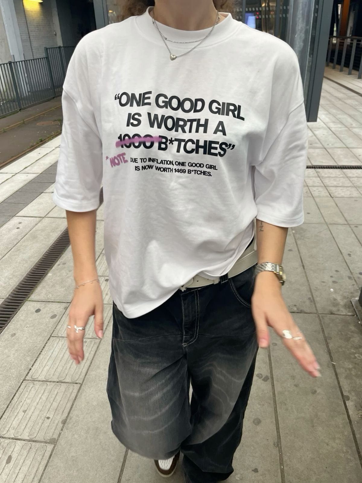 Person wearing a white oversized slogan t-shirt with bold black text and dark baggy pants.
