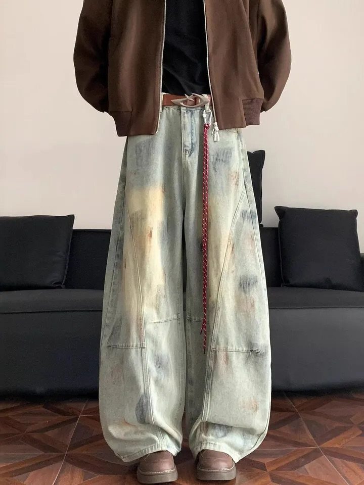 Person wearing oversized brown jacket and extremely wide-leg distressed denim jeans with a red chain.