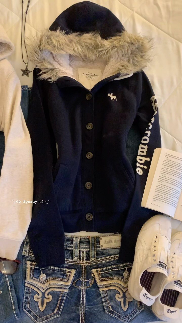 Navy blue hoodie, embroidered denim jeans, and white sneakers laid out on a white bedspread.