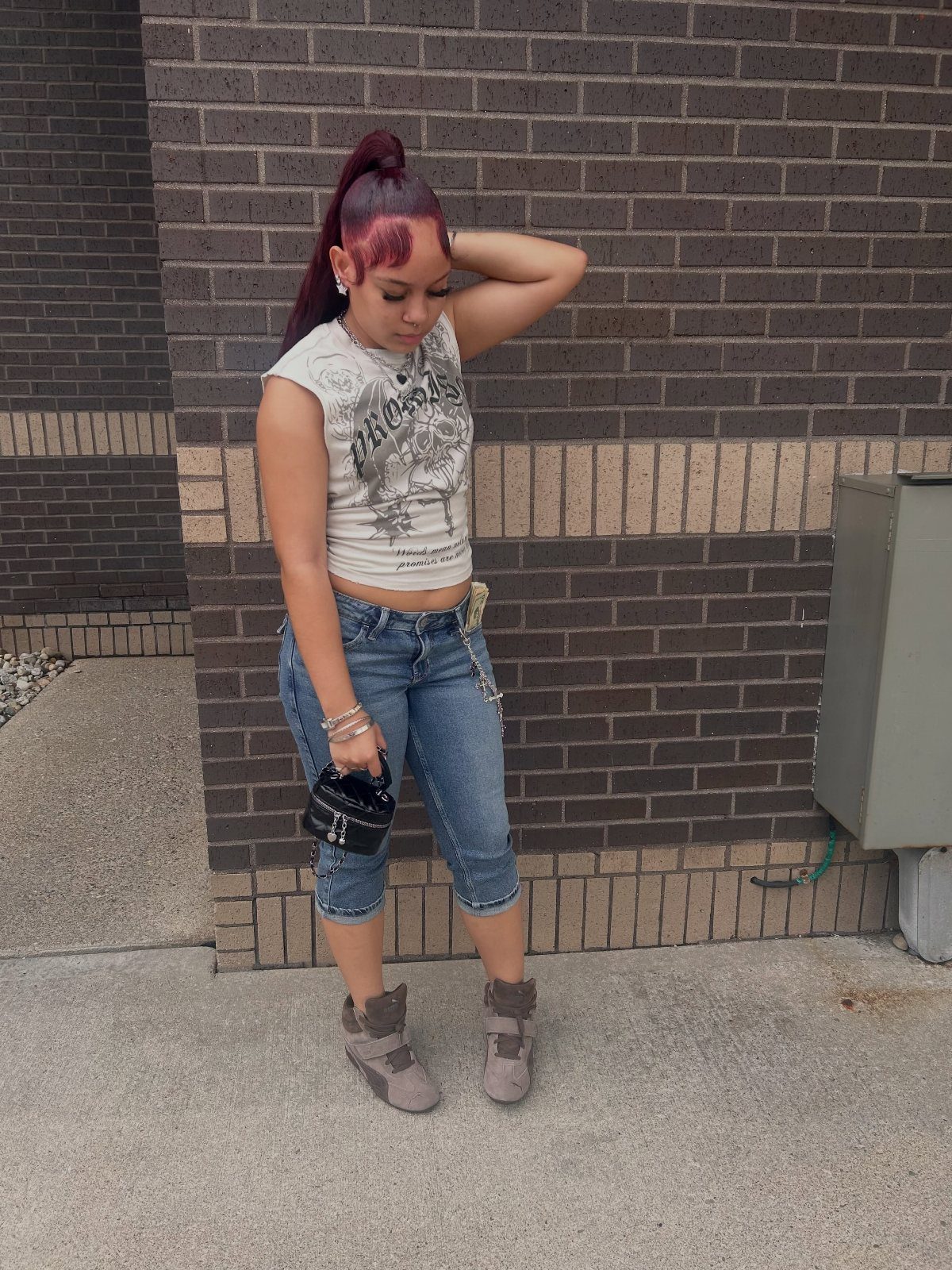 A woman in a graphic crop top, denim capris, and platform boots posing by a brick wall.