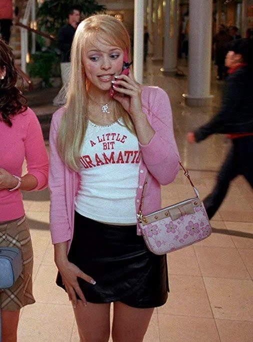 Blonde woman wearing a pink cardigan, white graphic tank top, and black leather mini skirt.