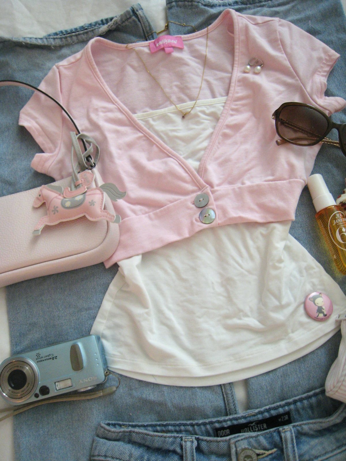 Pink cardigan and white tank top laid on denim with various Y2K accessories.