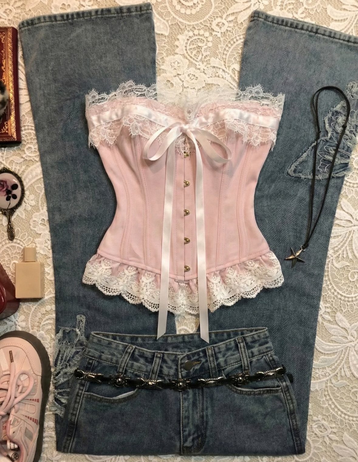 Pink lace corset and low-rise blue denim jeans laid on a white lace background.