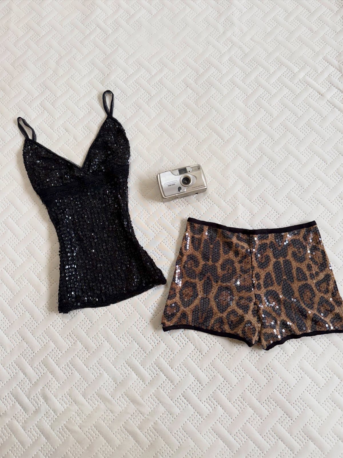 Black sequined camisole and leopard print sequined shorts laid next to a silver digital camera.