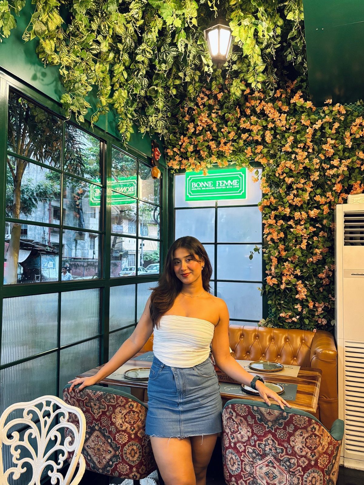 A woman wearing a white strapless tube top and denim mini skirt posing in a lush restaurant.