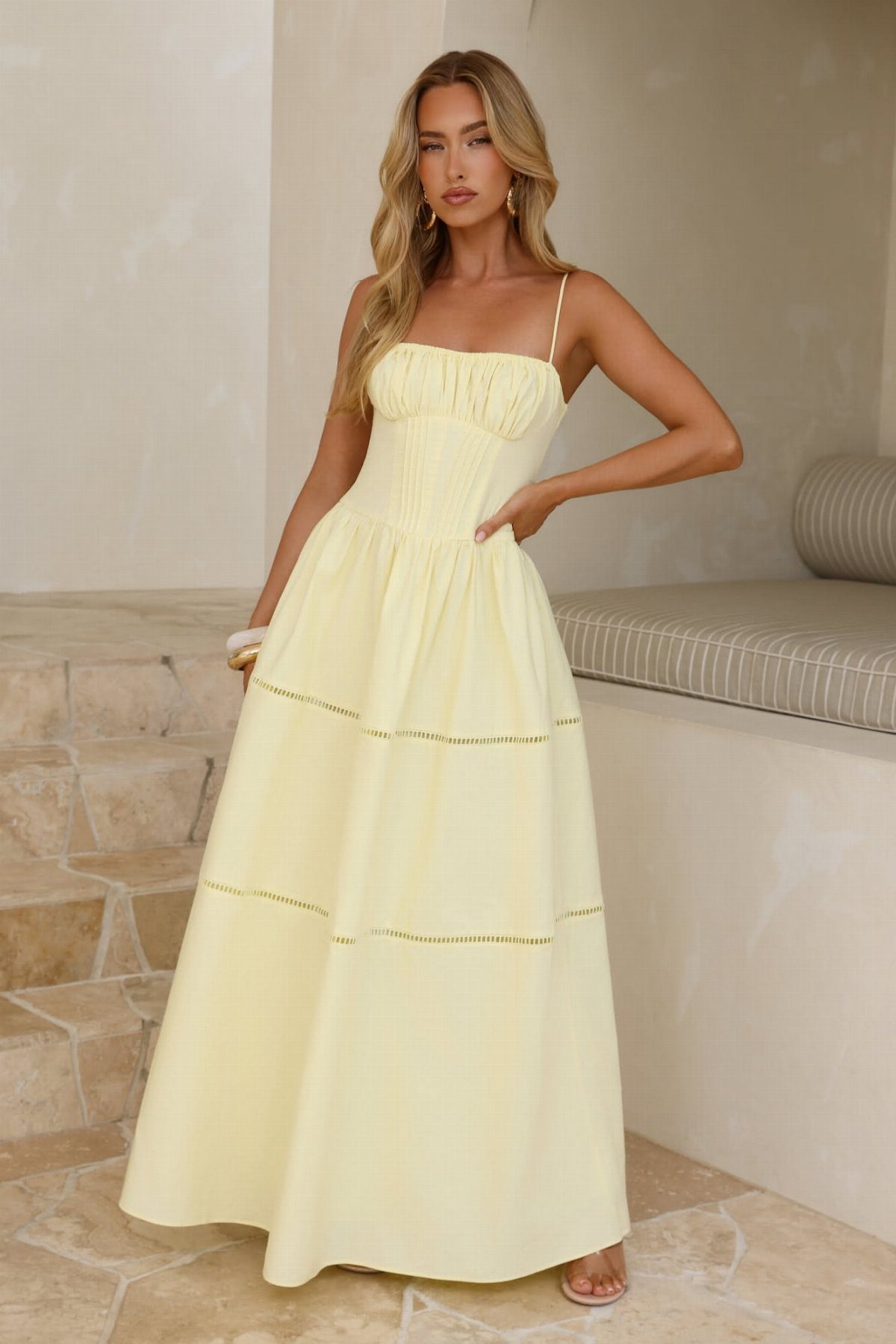 A woman posing in a pale yellow cotton maxi dress with eyelet lace detailing.