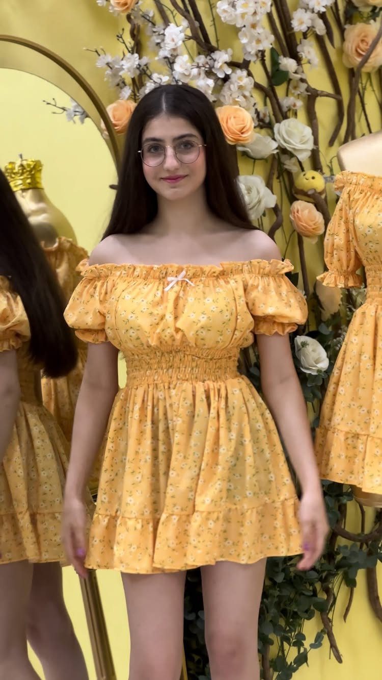 A young woman posing in a yellow floral off-the-shoulder smocked mini dress.